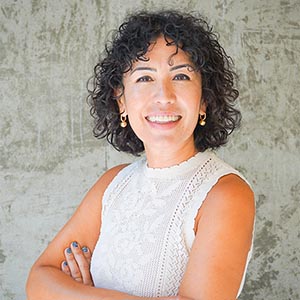 smiling woman with dark curly hair standing with rms crossed
