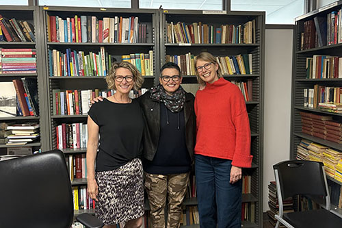 three smiling woman pose in front of bookcases